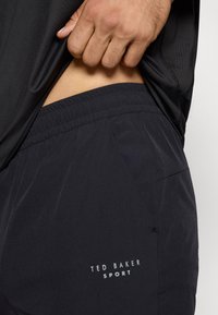 Melni sporta šorti, izgatavoti no viegla auduma, ar elastīgu jostasvietu un sānu kabatām. Baltā "TED BAKER SPORT" logo uz kājas.