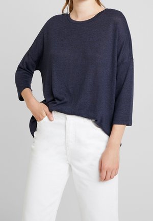 Dunkelblaues oversized Sweatshirt mit Dreiviertelärmeln, Rundhals und geripptem Muster, kombiniert mit weißen, hochgeschnittenen Jeans.