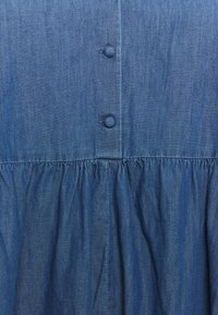 Jeansklänning med en sammandragna midja, med knappstängning och mjukt, texturerat tyg i en medelblå nyans.