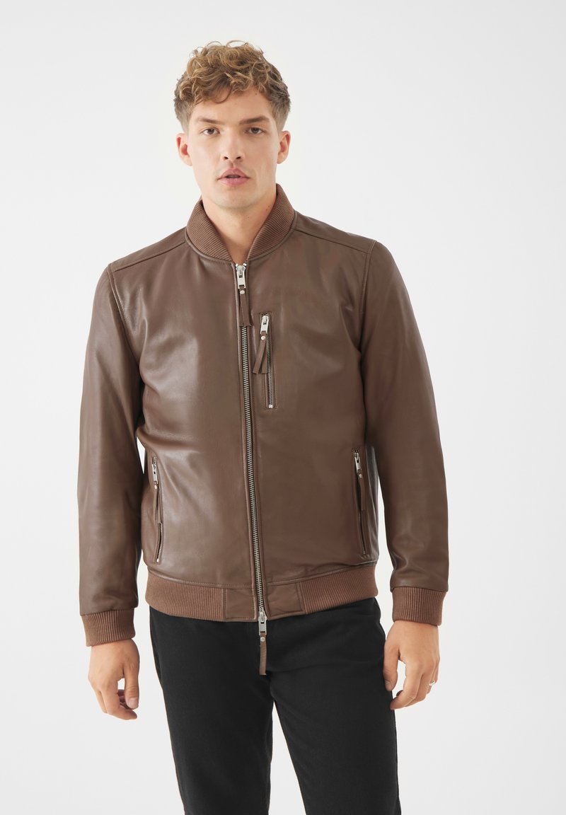 Giacca bomber in pelle marrone con chiusura a zip frontale, colletto e polsini a coste, tasche laterali e sul petto, texture liscia e design aderente.
