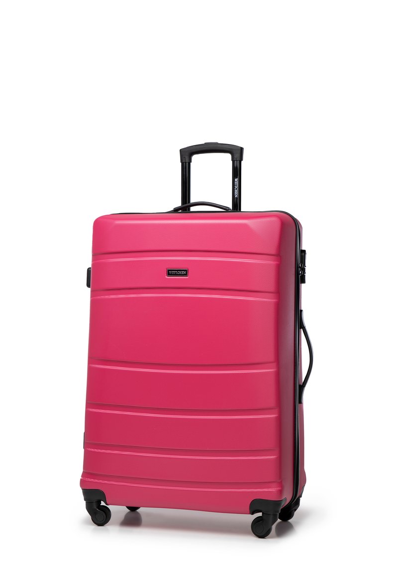 Grande valise rigide rose avec surface texturée, poignée télescopique noire, quatre roues et lignes horizontales subtiles.