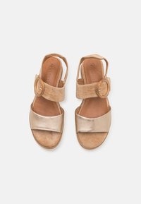 Paire de sandales beige et or métallisé à bouts ouverts avec brides à la cheville et larges boucles rondes, vues de dessus sur fond blanc.