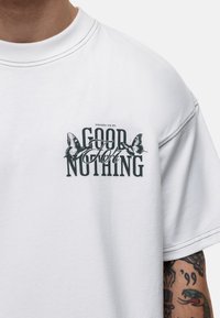 Biała bawełniana koszulka z krótkim rękawem i okrągłym dekoltem. Posiada czarny nadruk z motylami oraz tekstem "NIE DO NICZEGO."