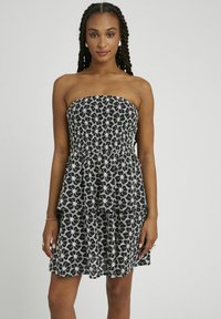 Robe sans bretelles noire et blanche avec un motif floral, corsage smocké et jupe à volants superposés. Fabriquée en tissu léger.