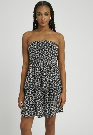 Robe sans bretelles noire et blanche avec un motif floral, corsage smocké et jupe à volants superposés. Fabriquée en tissu léger.