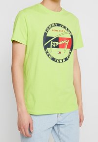 Neon zielona bawełniana koszulka T-shirt z okrągłym logo graficznym z napisem "Tommy Jeans" oraz "NEW YORK CITY" w kolorach granatowym i czerwonym. Krótkie rękawy.