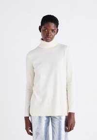 Gai bežs turtlenecks džemperis no mīksta adījuma, ar garām piedurknēm un ribotu maliņu, apvienots ar spīguļojošiem sudraba biksēm.