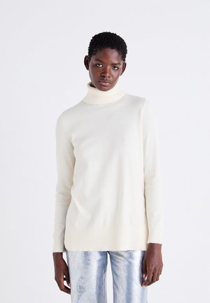 Light beige turtleneck sweater in soft knit fabric, featuring long sleeves and a ribbed hem, paired with shiny silver pants.