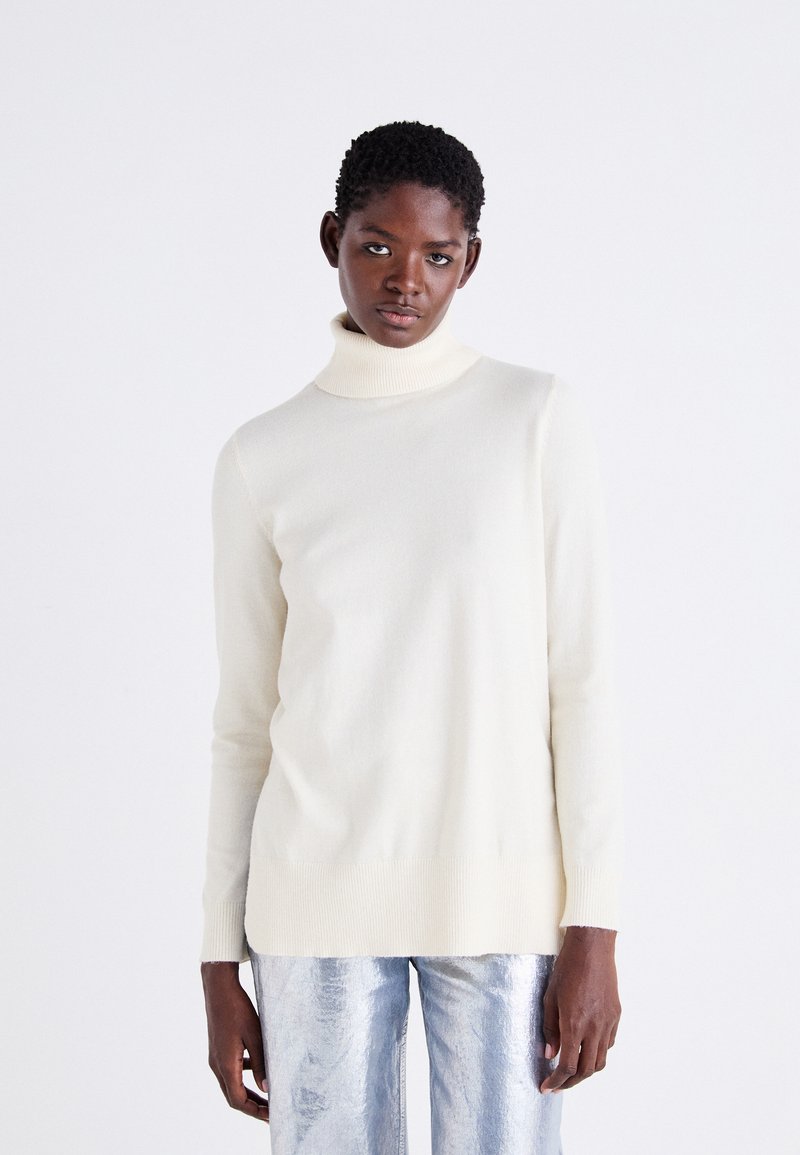 Gai bežs turtlenecks džemperis no mīksta adījuma, ar garām piedurknēm un ribotu maliņu, apvienots ar spīguļojošiem sudraba biksēm.