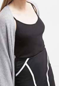 Černý top bez rukávů v kombinaci se šedým kardiganem; černé šaty mají bílé akcenty a přiléhavý střih. Hladká textilie.