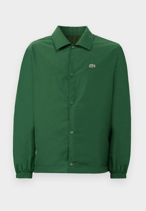 Veste verte avec un col, boutons-pression à l'avant et poignets élastiqués. Dotée d'un petit logo brodé sur la poitrine gauche. Texture lisse.