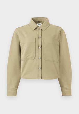 Chemise beige à manches longues avec boutons, col, deux poches plaquées devant, ourlet raccourci et détails de coutures visibles.
