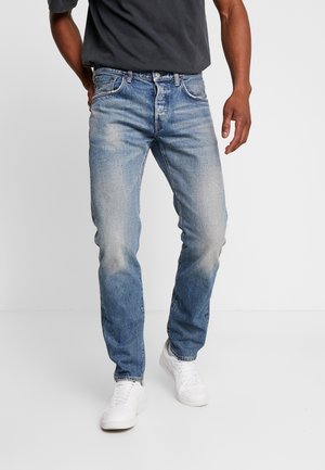 Light blue denim jeans featuring a straight-leg cut, faded areas, and subtle stitching details, paired with white sneakers and a dark t-shirt.