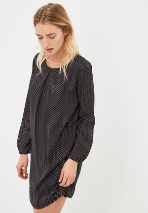 Vestido negro con lunares blancos, de mangas largas y escote redondo. Tejido suave con un corte holgado y un detalle de dobladillo ligeramente curvado.