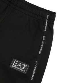 Pantaloni jogger neri realizzati in un tessuto morbido con una vita elasticizzata. Presentano un'etichetta con il marchio e una stampa logo verticale a contrasto lungo il lato.