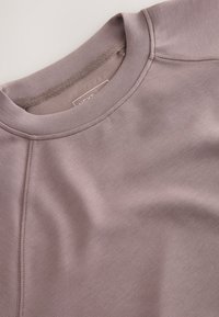 Felpa color malva chiaro con scollatura rotonda, maniche raglan e texture liscia. Include dettagli di cuciture sottili e un'etichetta interna.