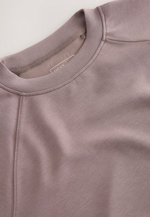 Hele lilla-sinine pusa, millel on ümmargune kaelus, raglaanvarrukad ja sile tekstuur. Sisaldab peeneid õmbluse detaile ning sees on silt.