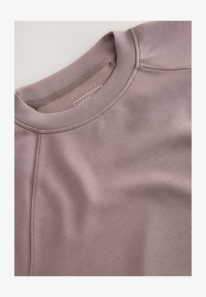 Hele lilla-sinine pusa, millel on ümmargune kaelus, raglaanvarrukad ja sile tekstuur. Sisaldab peeneid õmbluse detaile ning sees on silt.