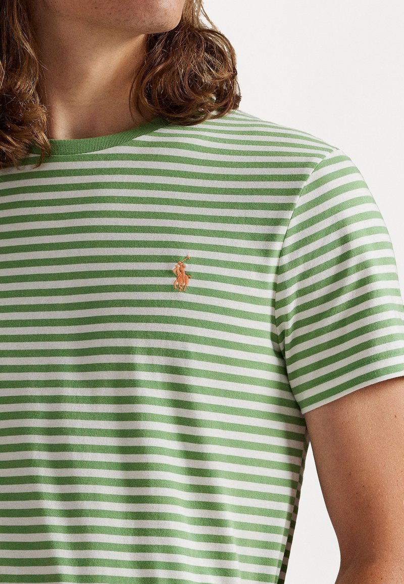 Grünes und weißes gestreiftes T-Shirt mit rundem Halsausschnitt. Hat ein kleines, orangefarbenes gesticktes Logo auf der Brust. Weicher Stoff.