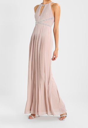 Robe plissée rose pâle sans manches avec taille et encolure ornées de perles, portée avec des talons ouverts argentés.