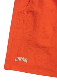 Oranger Stoff mit strukturiertem Finish, ausgestattet mit einer Seitentasche und dem Wort "UNFAIR" in weißer Schrift nahe dem Saum.