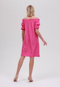 Rosa off-shoulder klänning med puffy ärmar, texturerat tyg, knälång, och slät finish. Bärs med nakna högklackade skor.
