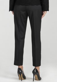 Czarne spodnie dopasowane wykonane z gładkiego materiału, charakteryzujące się zwężanym krojem, średnim stanem oraz bocznymi szwami; połączone z czarnymi szpilkami.