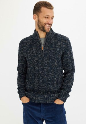 Pull en mailles torsadées bleu marine avec une fermeture éclair quart, présentant des motifs texturés. Assorti avec un sous-vêtement gris et un pantalon en velours côtelé bleu.