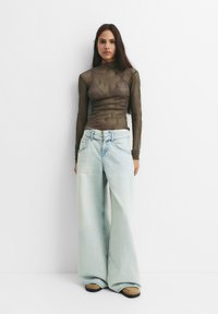 Gennemsigtig langærmet top i olivengrøn med tekstureret mønster, parret med vidde ben lys blå denimjeans og beige fodtøj.