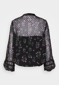 Blouse noire transparente à imprimé floral rose, pois, bordure en dentelle aux poignets et manches longues, vue de dos sur fond blanc.