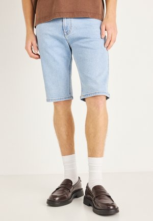 Pantalones cortos de mezclilla azul claro con corte recto y dobladillos enrollados, combinados con calcetines blancos con textura y mocasines marrón oscuro.