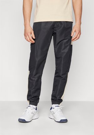 Pantaloni sport negri cu dungi crem pe laterale, talie elastică și manșete la glezne. Asortați cu adidași albi cu accente bleumarin.