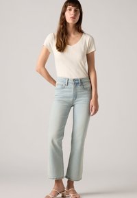 Un jean droit bleu clair associé à un haut blanc à manches courtes côtelé. Le jean est doté de poches classiques et d'une taille avec un bouton.