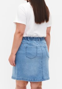 Ljust blå denimkjol med elastisk midja, två bakfickor och rak skärning. Slät textur med en fållad kant.