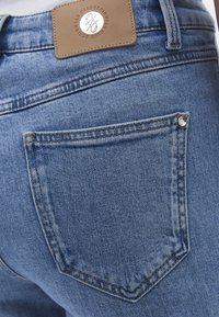 Nahaufnahme der Gesäßtasche einer blauen Denim-Jeans mit einem braunen Lederetikett der Marke, das oberhalb des Bunds aufgenäht ist.