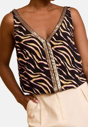 Vrouw draagt een zwarte mouwloze top met beige en roze zebrastripes en gouden paillettenkant, gecombineerd met hoog getailleerde crèmekleurige broek.