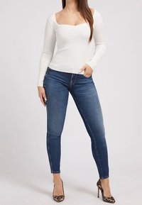 Haut blanc à manches longues à col carré, associé à un jean slim bleu foncé et des escarpins à imprimé léopard.