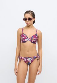 Bikini floral coloré avec une base violette, présentant un haut à torsion à l'avant et un bas ajustable avec liens sur les côtés, fabriqué en tissu lisse et extensible.