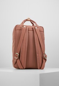 Różowy plecak z materiału z wyściełanymi paskami na ramiona i uchwytem górnym. Gładka tekstura i minimalistyczny design, z metalowymi akcentami.