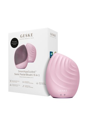 Brosse faciale sonique en silicone rose avec surface texturée à côté de sa boîte blanche étiquetée « GESKE SmartAppGuided 5 en 1 Brosse faciale sonique ».