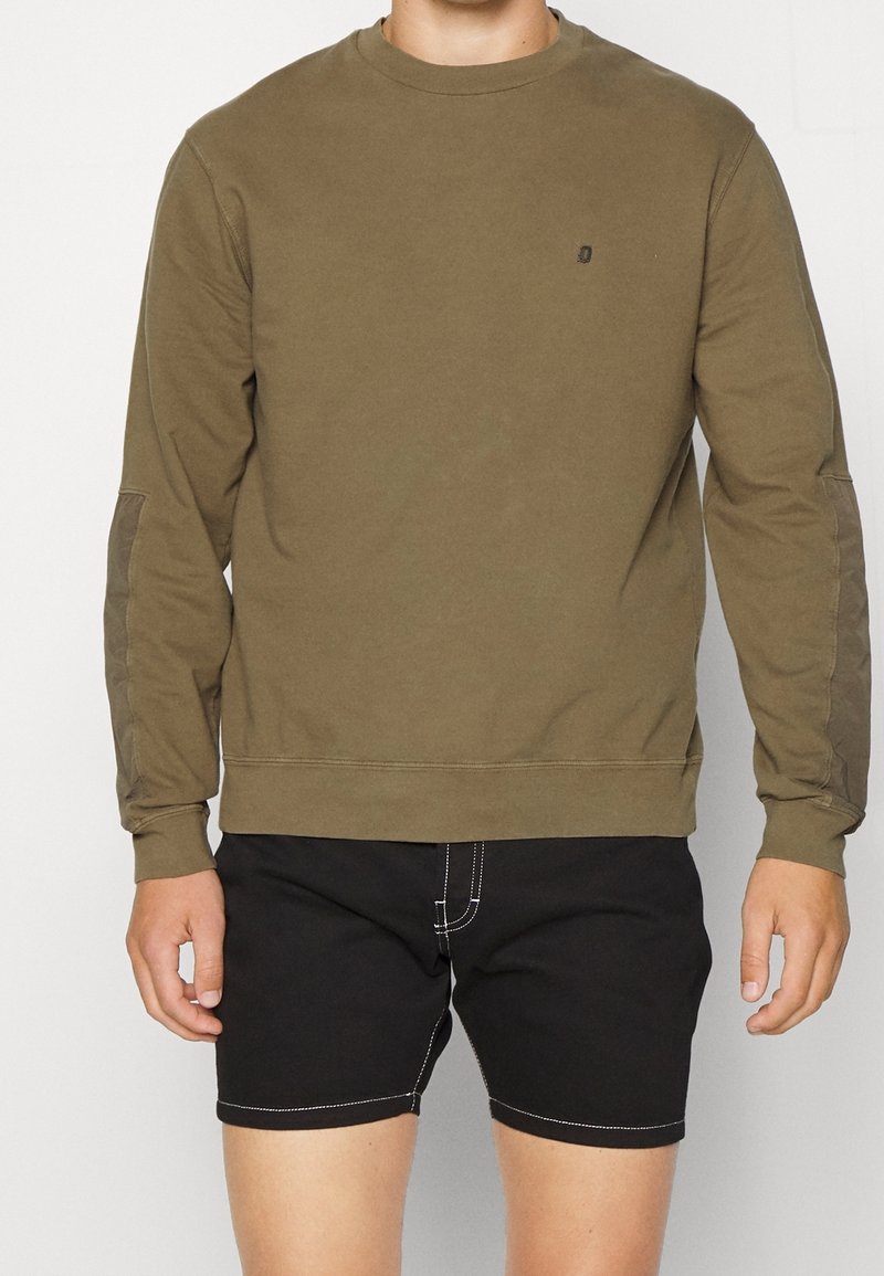 Olivgrön långärmad sweatshirt med rund halsringning, med en diskret logotyp på bröstet och sydda detaljer på axlarna.