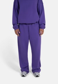 Lilla hettegenser og matchende joggebukser laget av mykt stoff. Antrekket har en avslappet passform og elastisk midjebånd. Sneakers synlige.