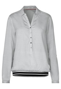 Chemise à manches longues en tissu léger, présentant un motif subtil de petits pois noirs sur fond blanc, une patte de boutonnage et un ourlet rayé.