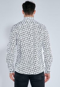 Weißes Langarmhemd mit einem geometrischen schwarz-weißen Muster. Standardkragen und geknöpfte Manschetten mit einer taillierten Passform.