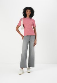Tricou cu dungi roșii și albe, cu mâneci scurte, asortat cu blugi gri evazați și teniși albi. Modelul ține o poșetă mică albă.
