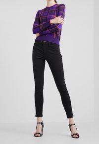 Suéter de punto morado a cuadros con puños y cuello acanalados, combinado con jeans negros ajustados y sandalias de tacón alto negras con tiras.