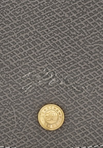 Grau strukturiertes Leder mit einem subtilen geometrischen Muster, ausgestattet mit einer goldenen Logo-Medaille und geprägten Details.