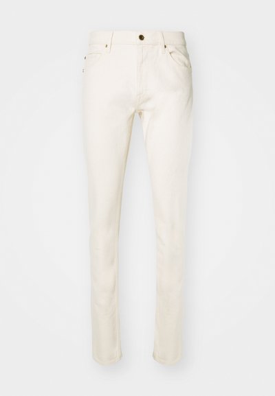Μπεζ τζιν από βαμβάκι με στενή εφαρμογή, διαθέτοντας μπροστινό κουμπί, πέντε τσέπες και διακριτές λεπτομέρειες ραφής. Λείος υφή και στενό πόδι.