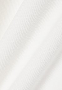 Weißer Stoff mit einem dezenten, strukturierten Muster aus kleinen, erhabenen sechseckigen Formen und sanften Falten, die weiche Schatten erzeugen.