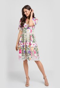 Sukienka z haftem kwiatowym w beżowym kolorze, z krótkimi rękawami, zdobiona wielokolorowymi kwiatami i warstwowym dołem. Posiada dekolt w kształcie litery V oraz wyraźną strukturę.